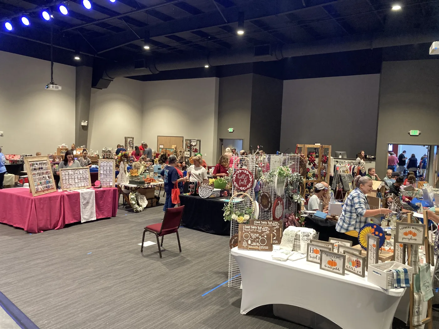 Rows of vendor tables with crafts, signs and seasonal decor in a large indoor hall