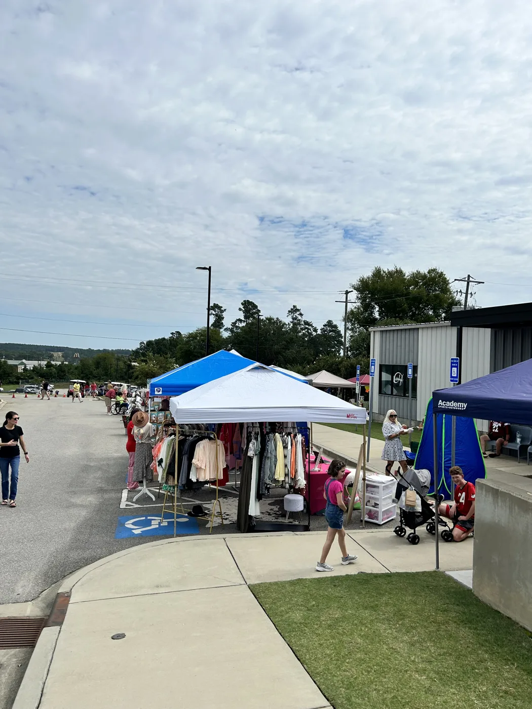 Pop-up tents with clothing racks and vendors set up along a parking lot under a cloudy sky