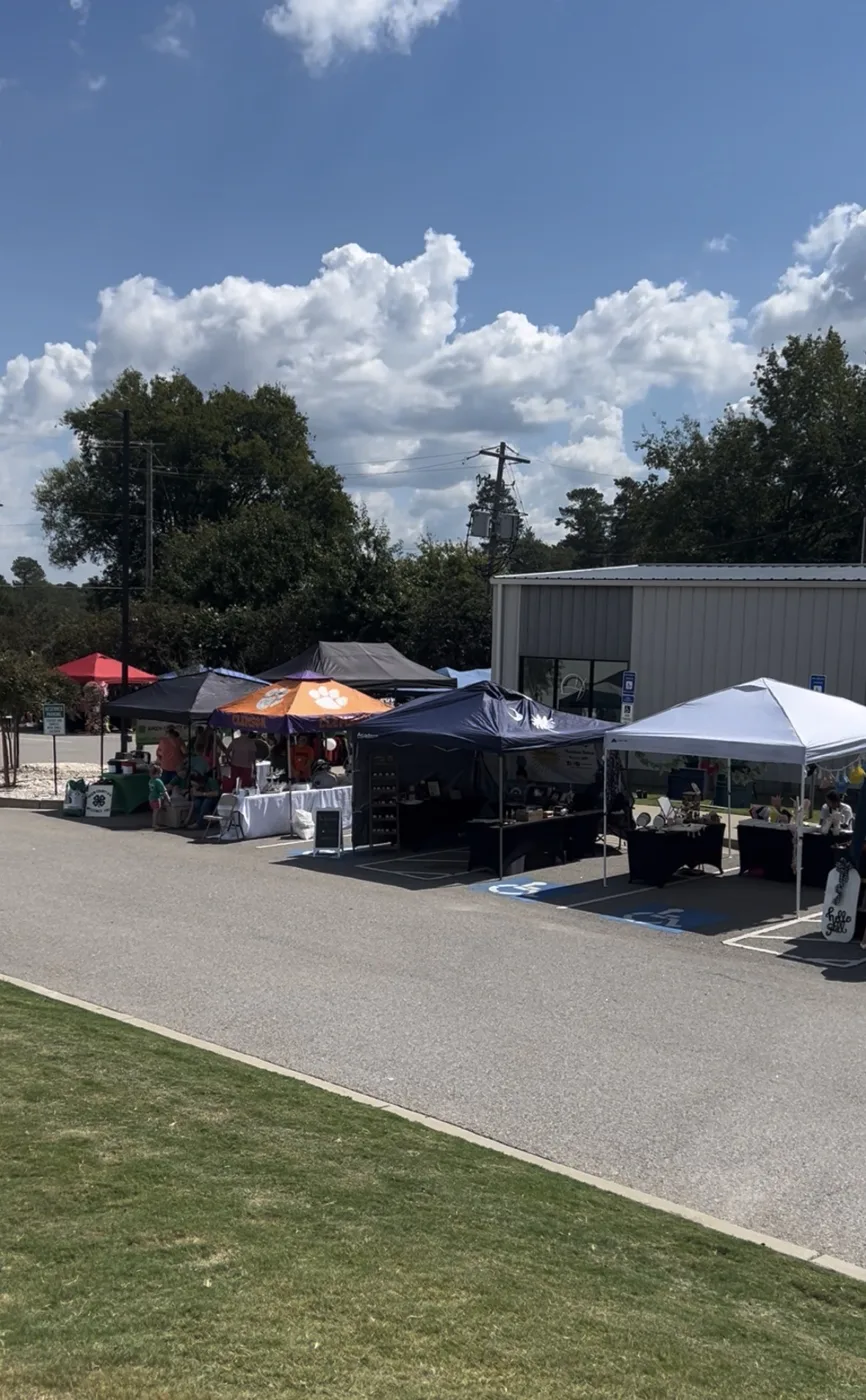 Vendor tents set up along a parking lot beside a metal building on a sunny day