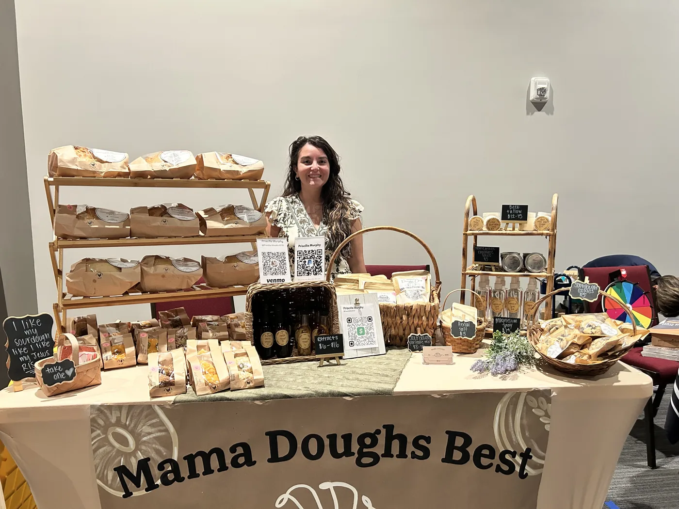 A sourdough bakery stand with loaves on wooden shelves and a Mama Doughs Best tablecloth