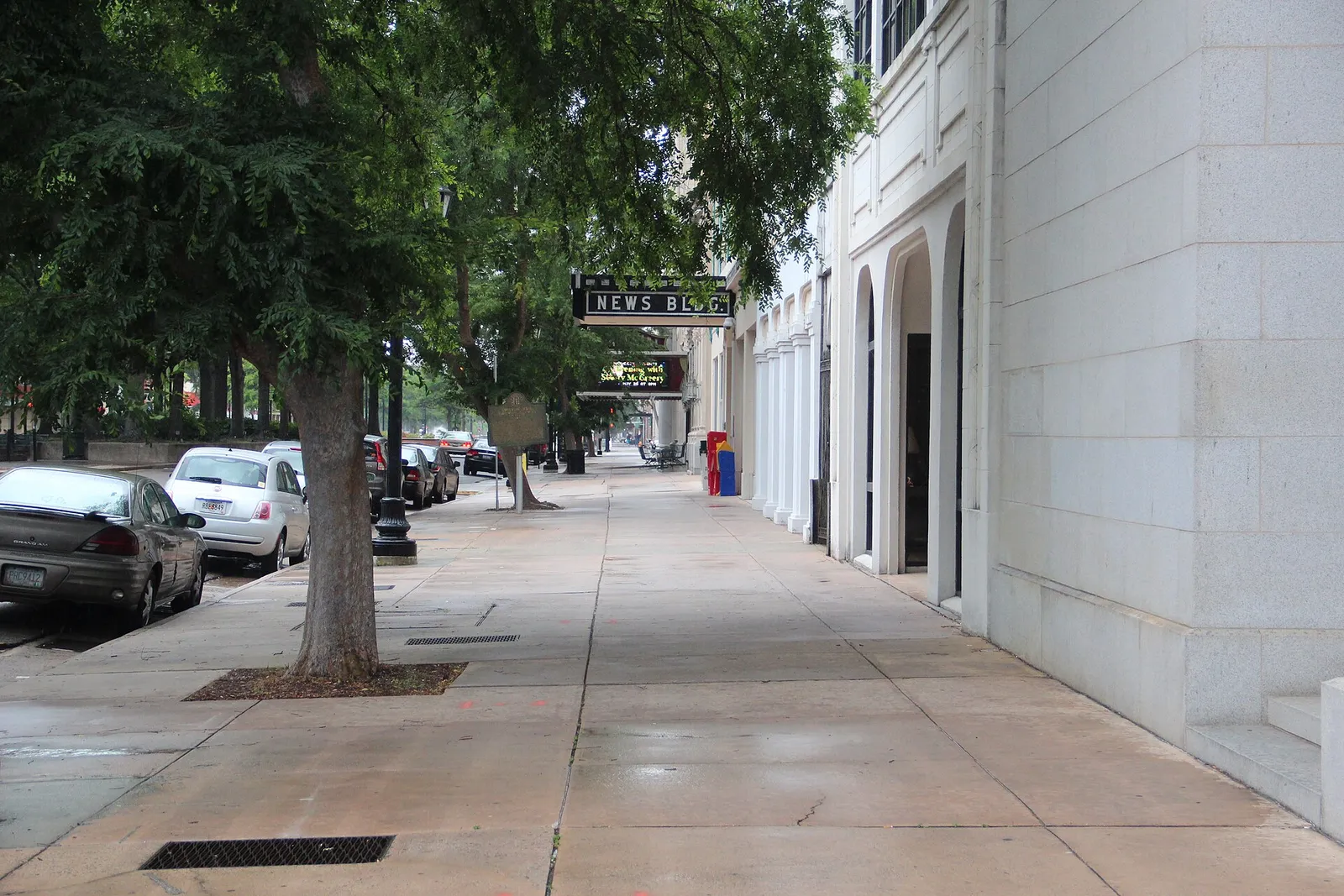 A tree-lined sidewalk on Broad Street in downtown Augusta, with sidewalk tables in the distance.
